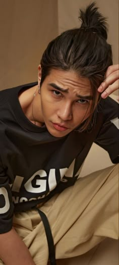 a young man sitting on the ground with his hair in a bun