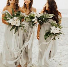 three bridesmaids walking on the beach with their bouquets in hand and laughing