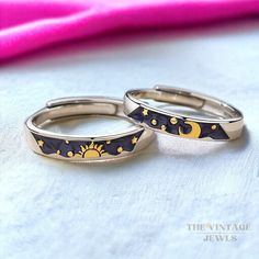 two gold rings with black and yellow designs are sitting on a white surface next to a pink towel