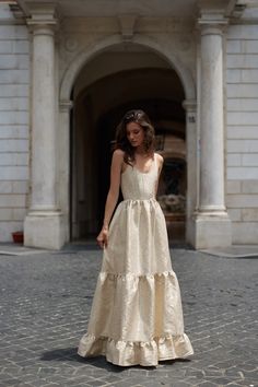 a woman in a white dress is standing on a cobblestone street and looking at the camera