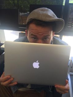 a man holding up an apple laptop in front of his face and looking at the camera