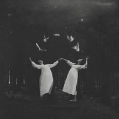 black and white photograph of two women standing in the woods with birds flying around her