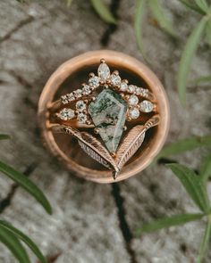 an engagement ring with a green stone surrounded by feathers and leaves on top of a rock