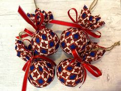 three red and blue ornaments hanging from twine on a white wooden table with ribbon