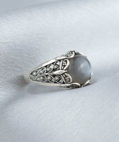 Make a statement with this stunning Handmade Filigree Art Gray Moonstone Gemstone Women Silver Cocktail Statement Ring. The elegant silver band beautifully complements the mesmerizing gray moonstone gemstone, making it the perfect addition to any jewelry collection. With intricate handcrafted details, this ring is sure to turn heads and spark conversations. Measuring 0.55 inches / 13.50 mm in length and width, this ring features a 10 mm cabochon round-cut Gray Moonstone Gemstone that adds a touc Celestial Style Silver Moonstone Ring With Gemstone Accents, Silver Moonstone Ring With Round Stone, Silver Moonstone Ring With Accent Stones, Elegant Moonstone Jewelry With Stone Setting, Elegant Sterling Silver Moonstone Ring With Stone Setting, Silver Oval Rings With Moon Phase, Silver Oval Ring With Moon Phase, Elegant Moonstone Ring For Anniversary, Elegant Moonstone Ring With Natural Stones For Anniversary