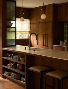 a kitchen with wooden cabinets and stools next to a counter top that has books on it