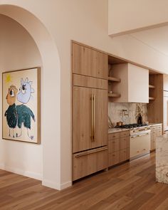 a kitchen with wood floors and white walls has an art piece on the wall above the refrigerator