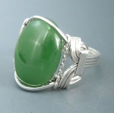 a large green stone ring on top of a gray surface with silver wire around it