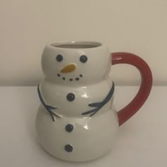 a ceramic snowman mug sitting on top of a white table next to a red handle