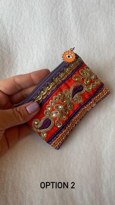 a hand holding an orange and purple purse on top of a white sheet with the words option 2 written below it