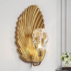 a gold scallop wall light on a white wall next to a vase with flowers