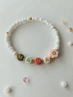 a white beaded bracelet with the word mama spelled in gold letters and two small beads