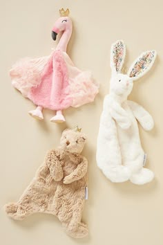 three stuffed animals are laying next to each other on a beige surface, one is wearing a pink dress and the other has a white bunny