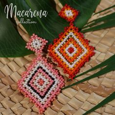 two beaded earrings sitting on top of a woven basket next to a plant with green leaves