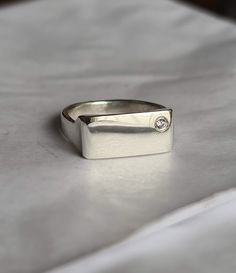 "Eleve su juego de meñique con nuestro exquisito anillo de plata rectangular. Este exclusivo anillo para el dedo meñique cuenta con un diseño contemporáneo que combina sin esfuerzo el minimalismo con un toque de lujo. El punto focal es una cautivadora zirconia, delicadamente colocada en la esquina, agregando un brillo sutil que llama la atención. Ya sea como una pieza independiente o como parte de su pila de anillos favorita, este accesorio es un testimonio de su refinado gusto e individualidad. Adopte la elegancia discreta con nuestro anillo plateado para el dedo meñique, un complemento imprescindible para su colección de joyas\"." Square Cut Diamond White Rings For Gifts, Silver Signet Ring With Single Diamond For Promise, Modern Rectangular Ring As A Gift, White Gold Sterling Silver Ring With Rectangular Stone, Rectangular White Gold Diamond Ring, Modern Silver Rings With Rectangular Stone, Minimalist Silver Rings With Diamond Accents, Modern Diamond White Signet Ring As Gift, Silver Formal Ring With Rectangular Stone