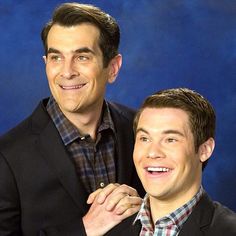 two men standing next to each other in front of a blue background, one is smiling at the camera