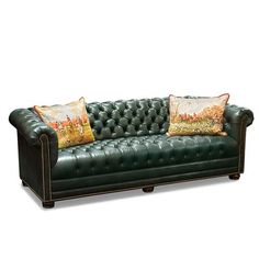 a green leather couch with two pillows on it's back and the seat upholstered