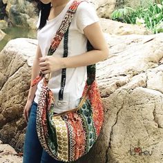 a woman is standing by some rocks and holding a purse