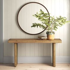 a wooden table with a potted plant on it and a round mirror above it