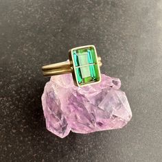 You won't be able to take your eyes off of this radiant cut green tourmaline ring. Aptly named, this stone radiates an array vibrant green hues. The double band compliments the crossbar and provides a luxurious contrast to the stone's geometric and longitudinal facets. A true one of a kind. 18k gold. 2.42 carat radiant cut green tourmaline. Size 7. Modern Green Jewelry With Accent Stones, Green Emerald Rectangular Stone Jewelry, Green Multi-stone Baguette Cut Rings, Green Radiant Cut Ring With Accent Stones, Green Radiant Cut Rings With Accent Stones, Radiant Cut Green Rings With Accent Stones, Green Baguette Cut Jewelry With Accent Stones, Green Jewelry With Radiant Cut Accent Stones, Modern Multi-stone Green Rings