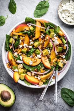 a salad with peaches, spinach and feta cheese in a white bowl