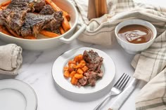 a table topped with meat and vegetables next to a bowl of sauce on top of a white plate