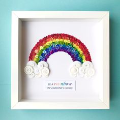 a rainbow made out of buttons in a white frame on a blue background with the words be a rainbow in someone's cloud