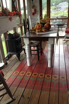 the porch is decorated with fall foliage and pumpkins on it's table, along with two chairs