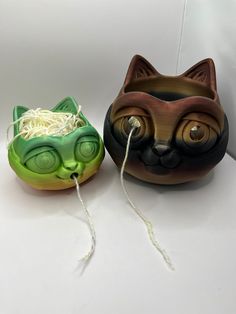 two ceramic bowls with cat faces and yarn in them on a white surface, one is green and the other is brown