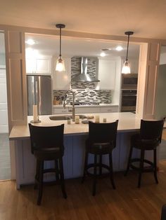 a kitchen with three bar stools next to an island in the middle of it