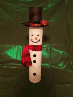 a snowman made out of toilet paper on a green sheeted surface with a top hat and scarf around his neck