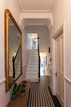 a hallway with black and white checkered flooring next to a wooden table topped with a potted plant