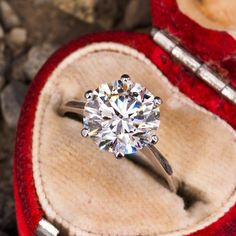 a diamond ring sits in an open red velvet case on top of rocks and stones