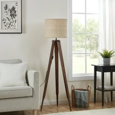 a living room with a white couch and wooden tripod floor lamp in front of a window