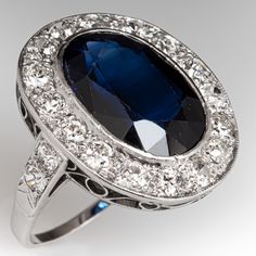 This beautiful ring is centered with one (1) laboratory grown sapphire set into a bezel setting. The sapphire is bordered with sixteen (16), bead set, old European/transitional brilliant/single cut diamonds. The shoulders of the ring are each accented with two (2), bead set, round transitional brilliant cut diamonds. The ring measures 20.2mm at the top, rises 5.3mm above the finger, tapering to 1.2mm wide and 0.6mm thick at the base of the shank. It is currently a size 5.5. Four of the melee diamonds are unnoticeably chipped. Classic Sapphire Ring With 17 Jewels In Platinum, Classic Oval Sapphire Ring, Vintage Sapphire Ring For Formal Occasions, Classic Formal Lab-created Sapphire Ring, Classic Sapphire Ring With 17 Jewels, Formal Sapphire Ring With 17 Jewels In Platinum, Classic Sapphire Ring With Halo Setting, Oval Platinum Diamond Ring With 17 Jewels, Classic Oval Sapphire Ring With Center Stone