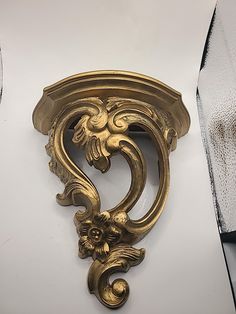 an ornately designed gold shelf bracket on a white wall