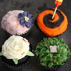 four decorated cupcakes sitting on top of a black table with white frosting