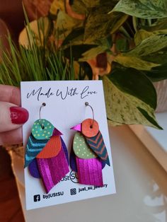 a pair of colorful bird shaped earrings sitting on top of a card next to a potted plant