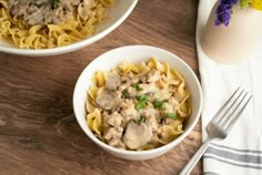 two white bowls filled with pasta and meat on top of a wooden table next to an egg