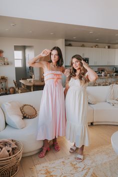 two women standing next to each other in front of a living room with white furniture