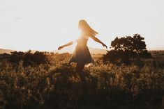 a woman standing in the grass with her arms spread out as the sun goes down