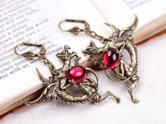 pair of dragon earrings on open book with red glass eyes in antique brass tone setting