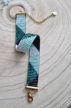 a blue and white beaded bracelet sitting on top of a wooden table next to a gold chain