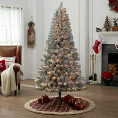 a white christmas tree in a living room next to a fireplace with stockings on it