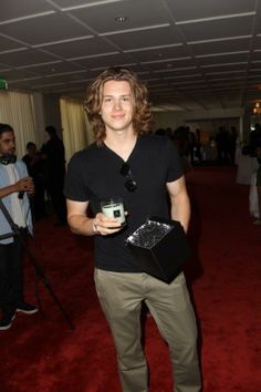 a young man is holding a cup in his hand while standing on the red carpet