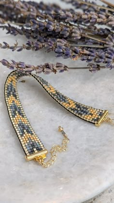 two pieces of jewelry sitting on top of a white marble table next to lavender flowers