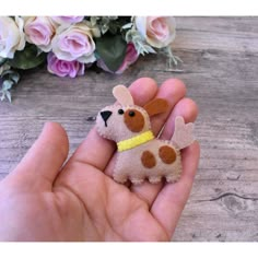 a hand holding a small toy dog in it's left hand next to flowers