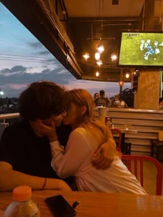 a man and woman sitting at a table with their arms around each other as they kiss