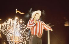 a man wearing a cowboy hat and holding a microphone in front of fireworks at night