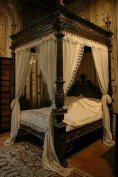 a canopy bed with white drapes on it's sides and an ornate wooden frame